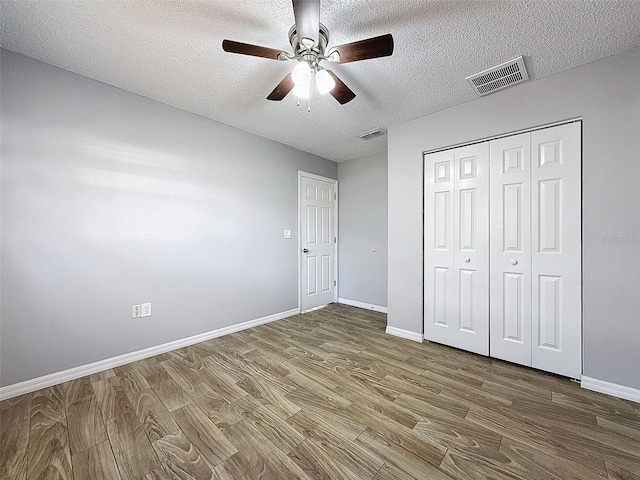 unfurnished bedroom featuring visible vents, a textured ceiling, baseboards, and wood finished floors