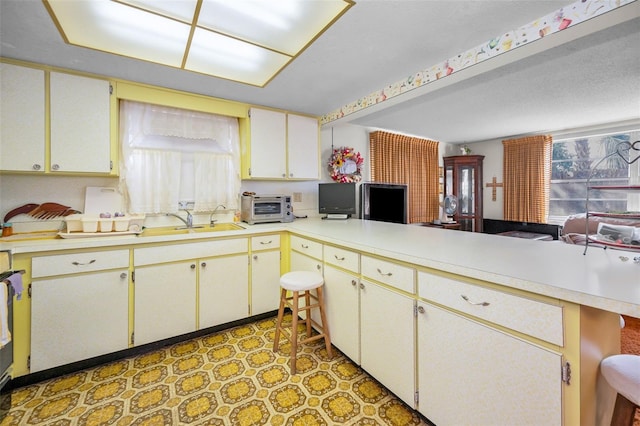 kitchen featuring light countertops, a peninsula, a sink, and light floors