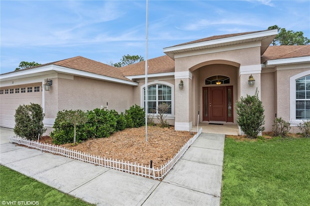 exterior space featuring an attached garage, a shingled roof, a lawn, and stucco siding