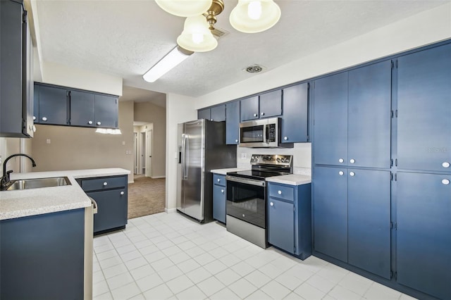 kitchen with sink, stainless steel appliances, a textured ceiling, and blue cabinets