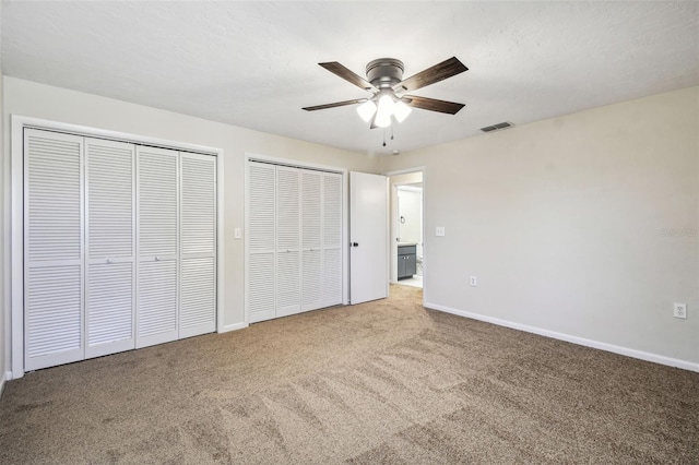 unfurnished bedroom featuring two closets, a textured ceiling, ceiling fan, and carpet flooring