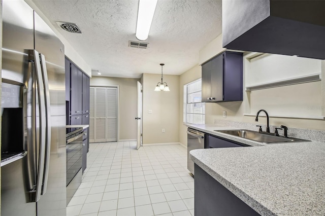 kitchen featuring sink, a textured ceiling, hanging light fixtures, light tile patterned floors, and stainless steel appliances