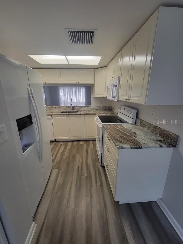 kitchen featuring sink, white appliances, white cabinetry, wood-type flooring, and kitchen peninsula