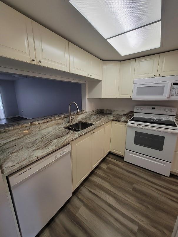 kitchen featuring dark hardwood / wood-style floors, sink, white cabinets, light stone counters, and white appliances