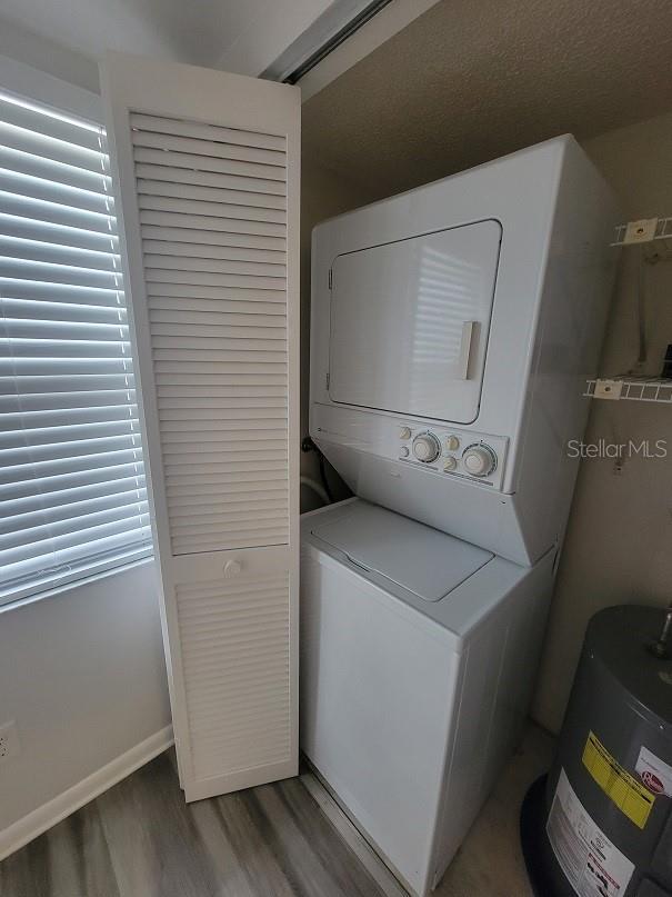 clothes washing area with hardwood / wood-style flooring, stacked washer / drying machine, and electric water heater