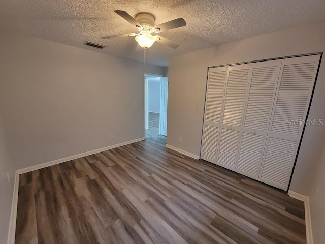 unfurnished bedroom with ceiling fan, dark hardwood / wood-style floors, a closet, and a textured ceiling