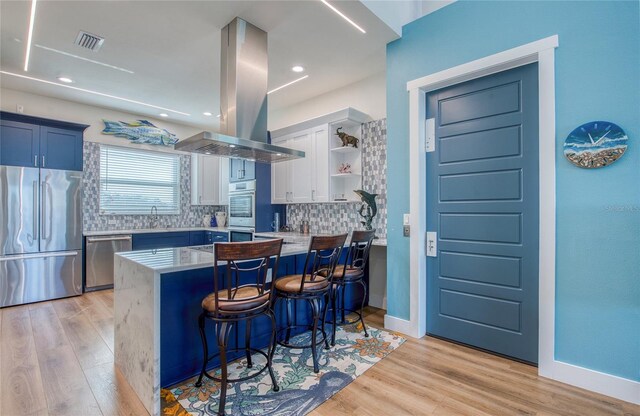 kitchen with island exhaust hood, blue cabinets, stainless steel appliances, kitchen peninsula, and a breakfast bar area