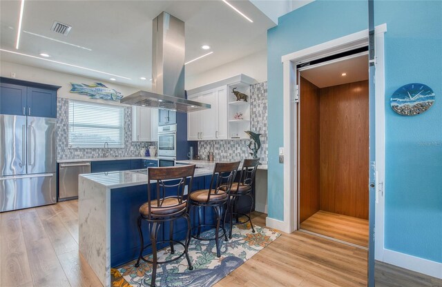 kitchen featuring island exhaust hood, blue cabinetry, a kitchen breakfast bar, stainless steel appliances, and kitchen peninsula