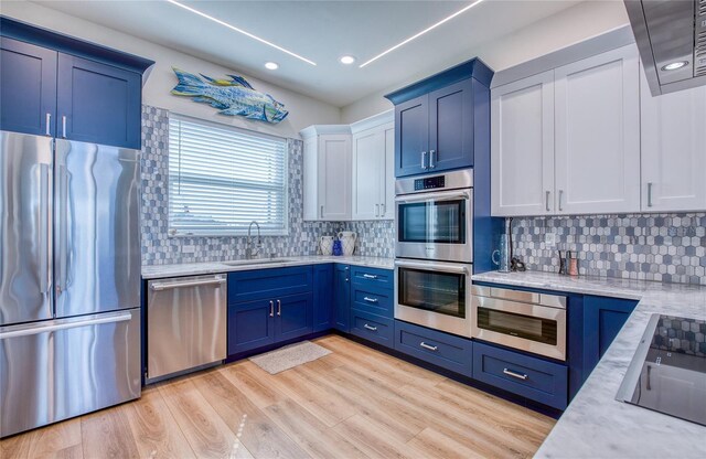 kitchen with appliances with stainless steel finishes, sink, light stone counters, light hardwood / wood-style floors, and tasteful backsplash