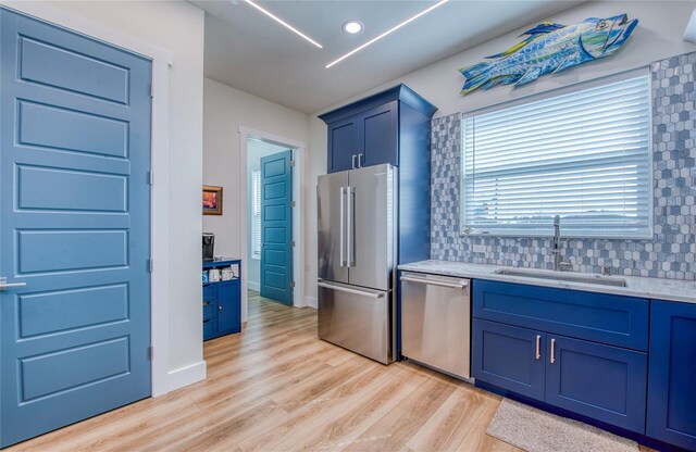 kitchen with light hardwood / wood-style flooring, stainless steel appliances, blue cabinets, backsplash, and sink