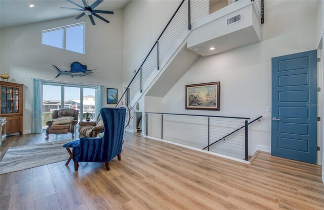 living area featuring a towering ceiling, ceiling fan, and light hardwood / wood-style flooring