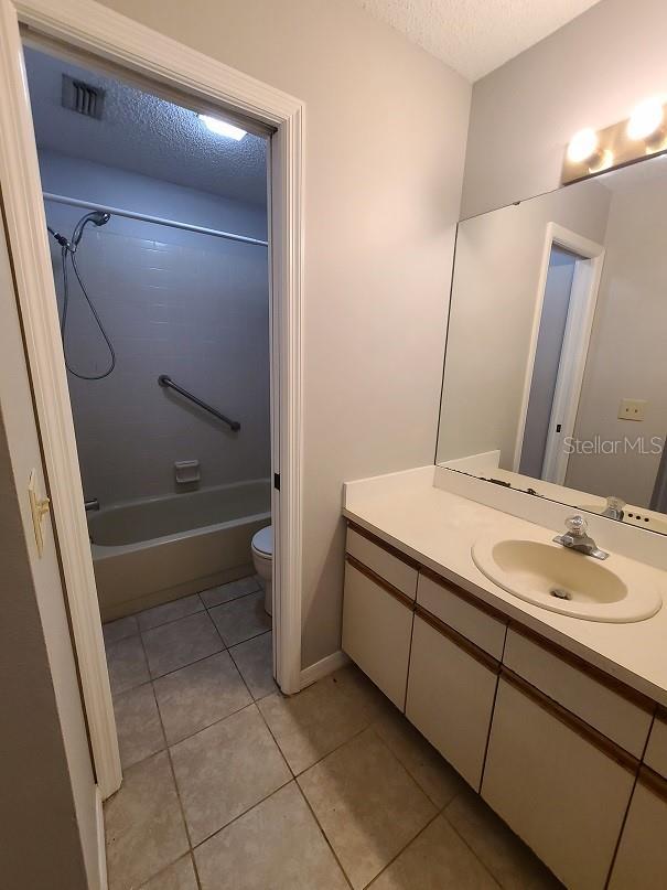 full bathroom featuring shower / bathtub combination, vanity, a textured ceiling, toilet, and tile patterned floors