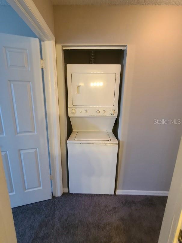 clothes washing area with stacked washer and dryer and dark colored carpet