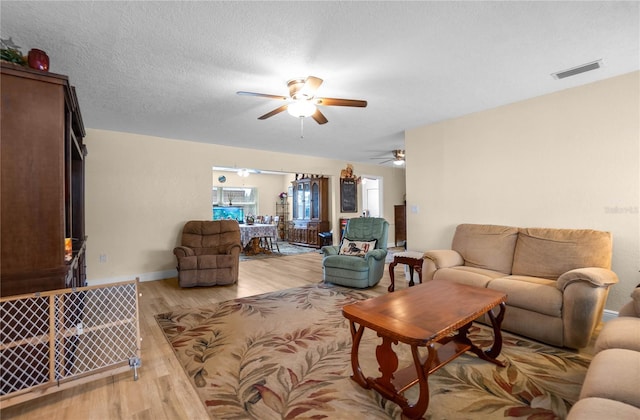 living room featuring ceiling fan, a textured ceiling, and light hardwood / wood-style floors