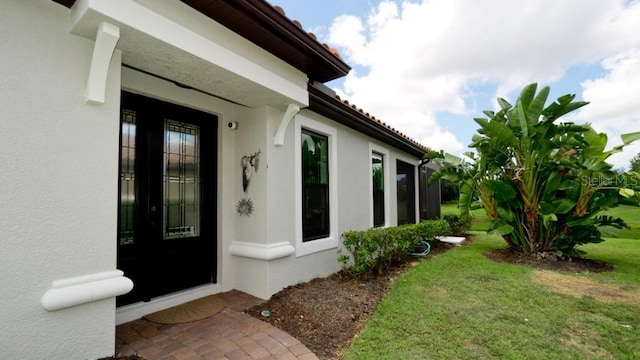 entrance to property featuring a lawn and stucco siding