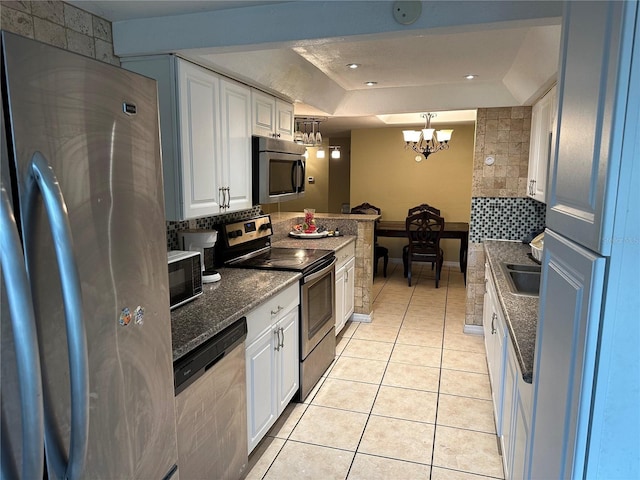 kitchen featuring appliances with stainless steel finishes, pendant lighting, white cabinetry, light tile patterned floors, and a tray ceiling