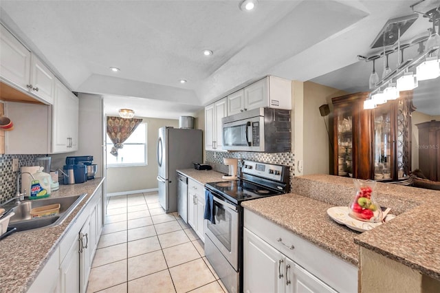 kitchen with a sink, stainless steel appliances, a raised ceiling, and white cabinetry