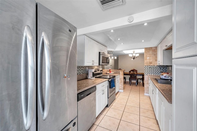 kitchen with stainless steel appliances, stone counters, white cabinetry, a notable chandelier, and light tile patterned flooring