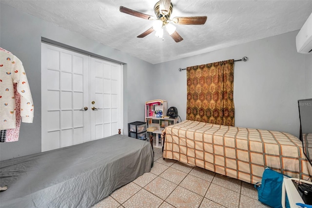 bedroom with a textured ceiling, light tile patterned floors, a wall mounted AC, and a ceiling fan