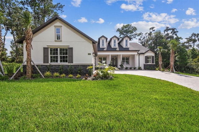 view of front of home with a porch, stone siding, decorative driveway, stucco siding, and a front yard