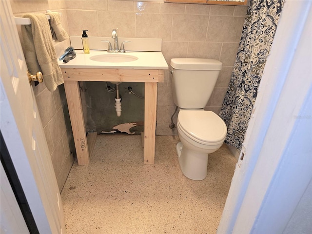 bathroom with toilet, sink, and tile walls