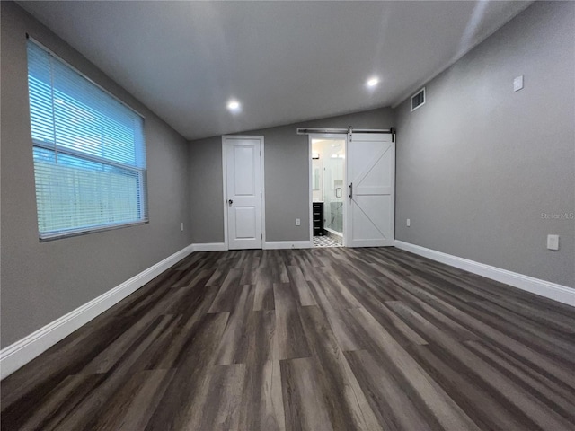 spare room featuring vaulted ceiling, a barn door, and dark hardwood / wood-style flooring