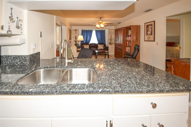 kitchen with dark stone countertops, sink, kitchen peninsula, and white cabinets