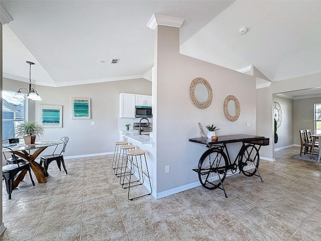 interior space with white cabinetry, decorative light fixtures, ornamental molding, vaulted ceiling, and a breakfast bar area