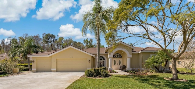 mediterranean / spanish house featuring a tile roof, stucco siding, concrete driveway, a front yard, and a garage