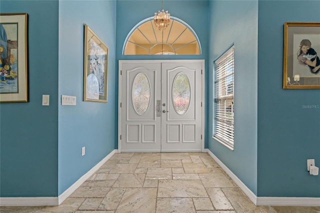 entryway featuring baseboards, a chandelier, and stone tile flooring