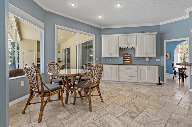 kitchen with baseboards, dark countertops, crown molding, stone tile flooring, and white cabinetry