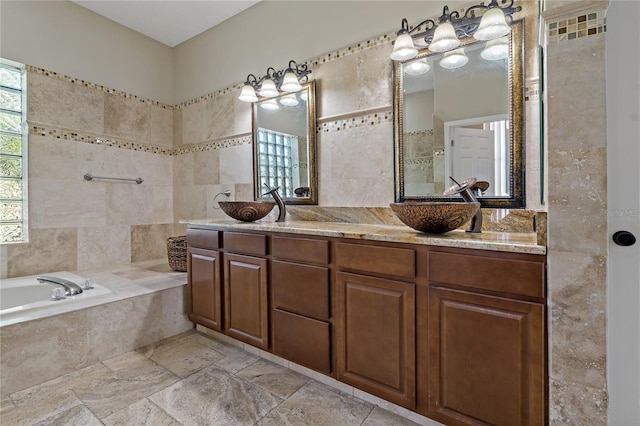 bathroom with a garden tub, tile walls, double vanity, stone tile flooring, and a sink