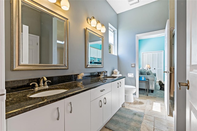 ensuite bathroom featuring toilet, double vanity, visible vents, and a sink