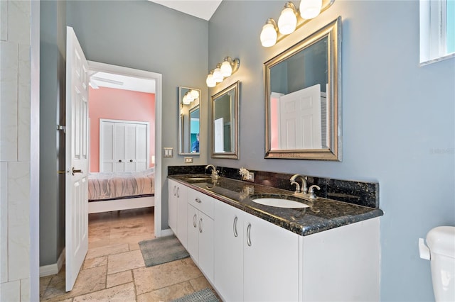 full bath featuring a sink, double vanity, baseboards, and stone tile flooring