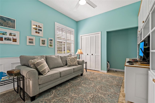 living area featuring ceiling fan, a wainscoted wall, and a textured ceiling