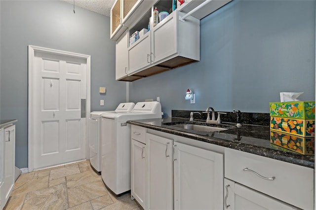 clothes washing area featuring a textured ceiling, stone tile floors, separate washer and dryer, a sink, and cabinet space