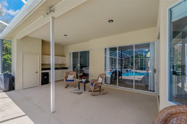 view of patio featuring a sink, glass enclosure, exterior kitchen, and area for grilling