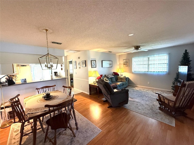 dining room with ceiling fan with notable chandelier, hardwood / wood-style flooring, and a textured ceiling