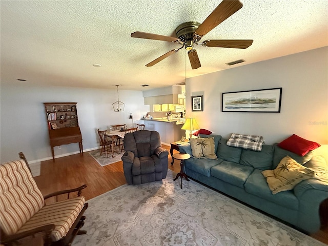 living room featuring light wood-type flooring, ceiling fan, and a textured ceiling