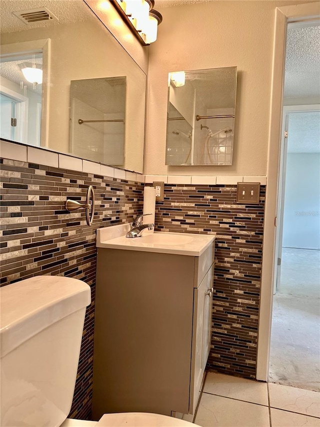 bathroom with tile walls, tile patterned flooring, vanity, toilet, and a textured ceiling