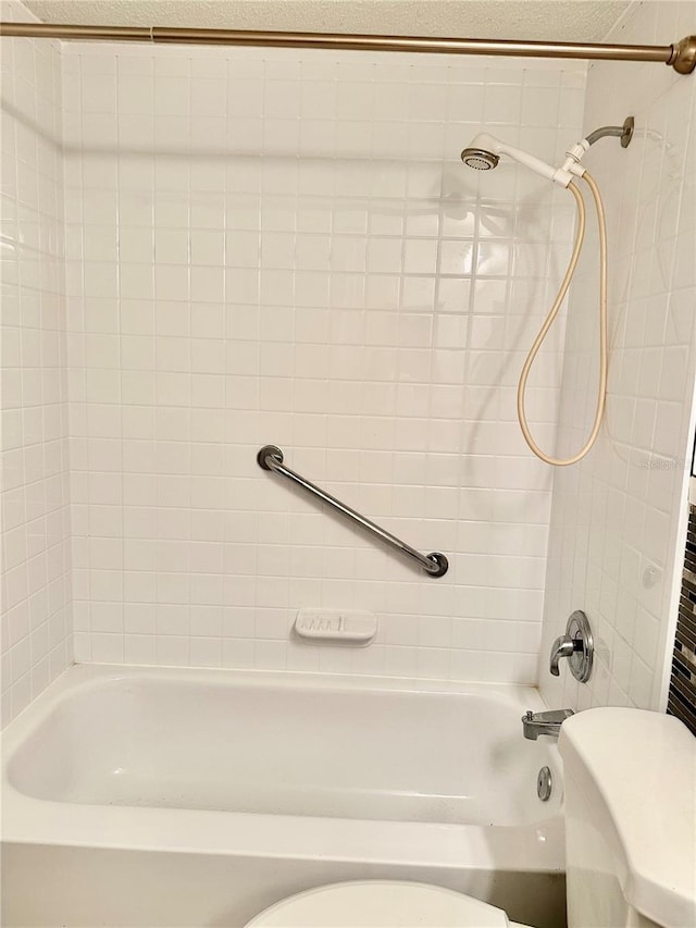 bathroom featuring tiled shower / bath, a textured ceiling, and toilet