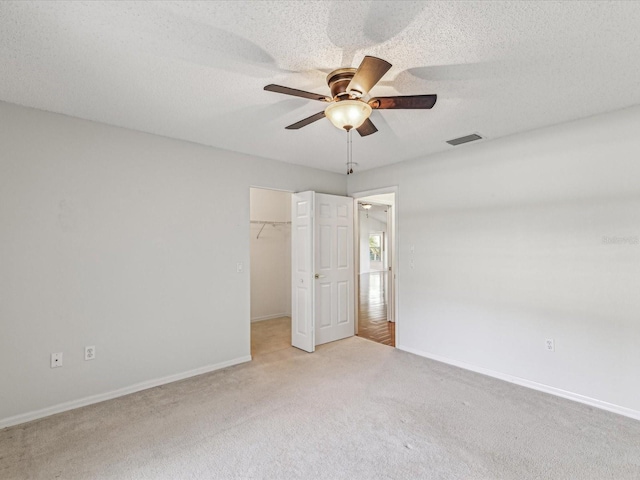 unfurnished bedroom with light carpet, baseboards, a walk in closet, and a textured ceiling