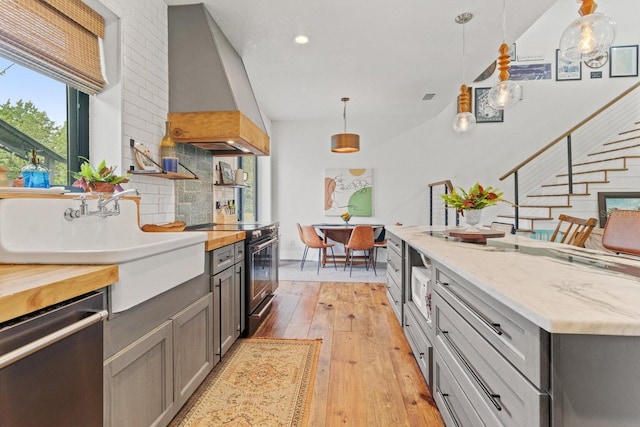 kitchen with gray cabinets, light wood-style floors, premium range hood, and stainless steel appliances