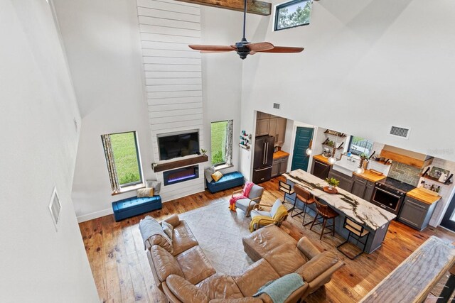 living area with ceiling fan, a high ceiling, visible vents, and light wood-type flooring