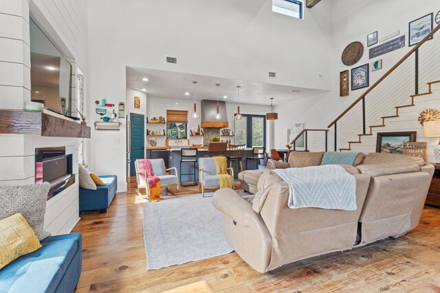 living area featuring stairway, light wood-style floors, visible vents, and a towering ceiling