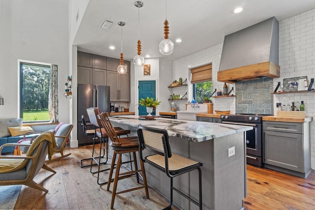 kitchen featuring visible vents, wall chimney range hood, gray cabinets, appliances with stainless steel finishes, and open shelves