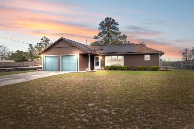 ranch-style home featuring driveway, an attached garage, fence, a yard, and roof mounted solar panels