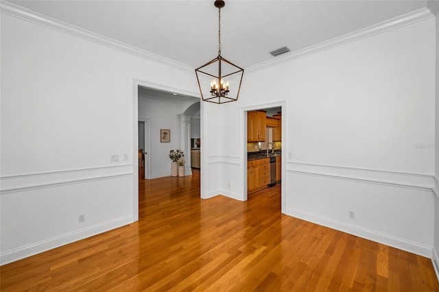 unfurnished dining area featuring arched walkways, a sink, wood finished floors, visible vents, and crown molding