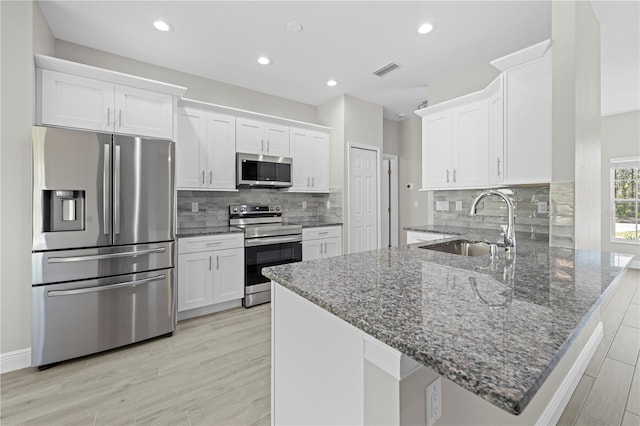 11345 Thrasher Ave, Weeki Wachee, FL 34614 - kitchen featuring stainless steel appliances, a peninsula, white cabinetry, a sink, and stone countertops