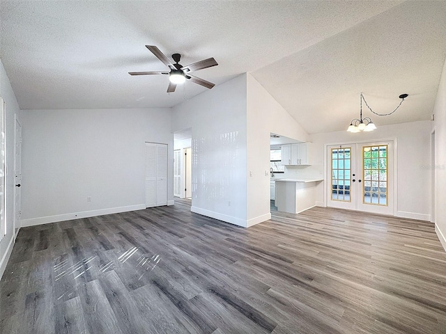 unfurnished living room with lofted ceiling, a textured ceiling, dark hardwood / wood-style floors, ceiling fan with notable chandelier, and french doors